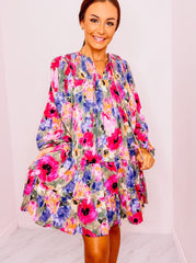 Floral print long sleeve tiered mini dress featuring smocking detail at front. Self-tie at front. Pockets at side