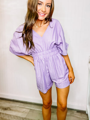 Lavender v-neck pleated romper with front pockets and elastic waistband.